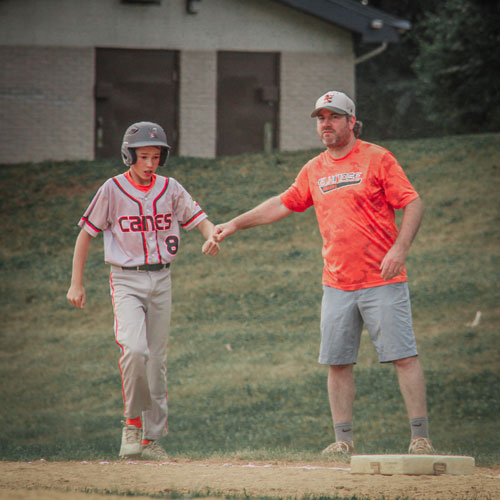 An Elkridge Hurricanes base runner gets a pound from the first base coach as he returns to first base after a single.
