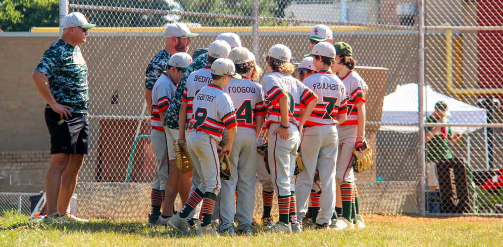 The Gray team huddles around the coaching staff near the dugout for a team talk.