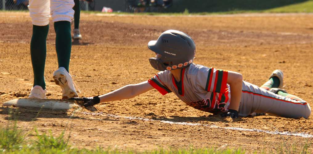Baserunner Ryan Schwaab lies on his stomach with his hand outstretched touching first base after diving back into the bag during a pickoff attempt.