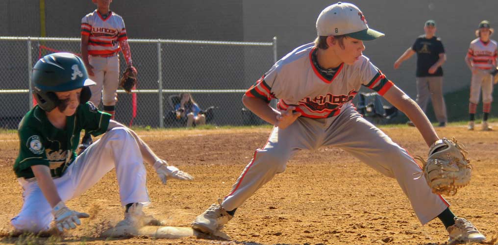 First baseman Camden Bednar outstretched, picks a ball thrown by an infielder, narrowly beating the sliding batter to first for the out.